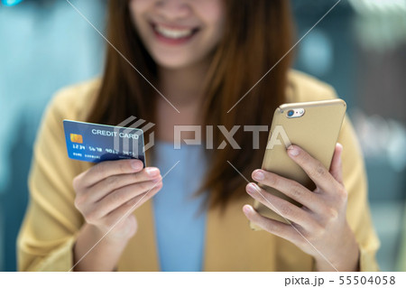 Closeup Asian woman using credit card with mobile for online shopping in department store over the clothes shop store background, technology money wallet and online payment concept, credit card mockup Closeup Asian woman using credit card with mobile for online shopping in department store over the clothes shop store background, technology money wallet and online payment concept, credit card mockup 55504058