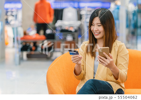 Asian woman using credit card with mobile phone for online shopping in department store over the clothes shop store background, technology money wallet and online payment concept, credit card mockup 55504062