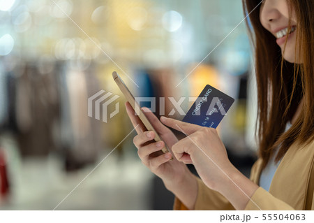 Closeup Asian woman using credit card with mobile for online shopping in department store over the clothes shop store background, technology money wallet and online payment concept, credit card mockup 55504063