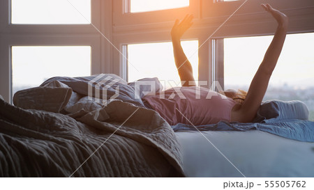 Beautiful romantic brunette woman lying on the bed stretches up in her room hiding blanket. during Beautiful romantic brunette woman lying on the bed stretches up in her room hiding blanket. during 55505762