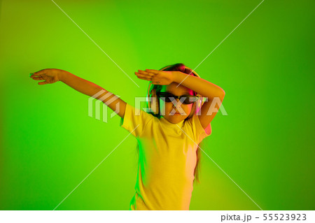 Portrait of little girl in headphones on green background in neon light 55523923