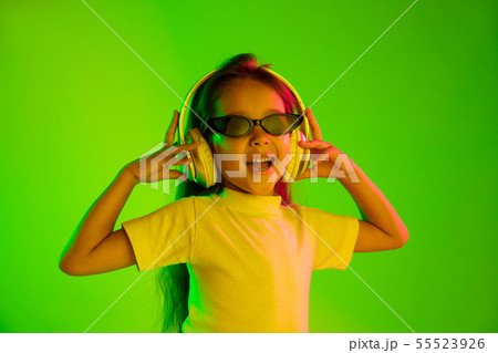 Portrait of little girl in headphones on green background in neon light 55523926