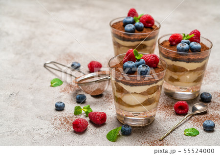 Classic tiramisu dessert with blueberries and raspberries in a glass and strainer with cocoa powder Classic tiramisu dessert with blueberries and raspberries in a glass and strainer with cocoa powder 55524000