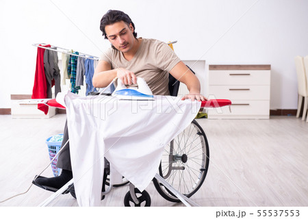 Young man in wheel-chair doing ironing at home 55537553