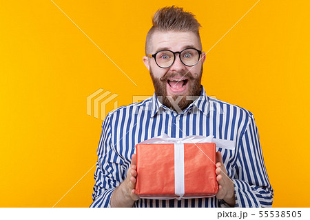 Surprised young hipster man with mustache and beard in surprise unpacks a red box with gifts on a Surprised young hipster man with mustache and beard in surprise unpacks a red box with gifts on a 55538505