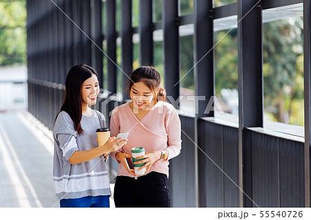 Young Asian business women talking and showing phone screen in office building in casual wear Young Asian business women talking and showing phone screen in office building in casual wear 55540726