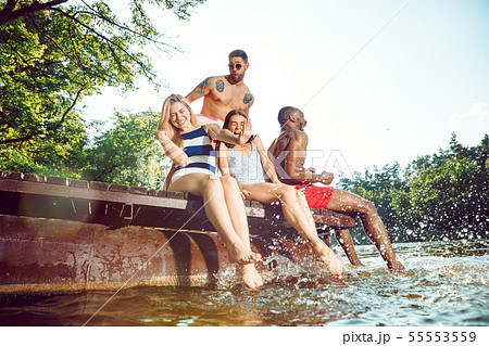 Group of happy friends having fun while sitting and laughting on the pier on river Group of happy friends having fun while sitting and laughting on the pier on river 55553559