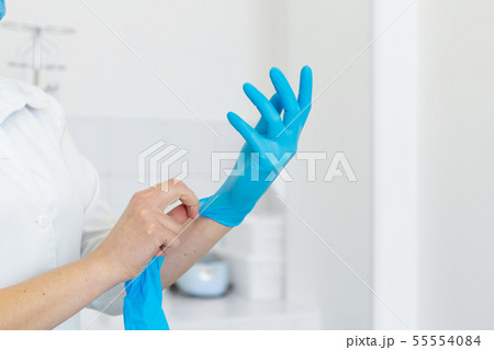 Nurse in scrub and mask puts gloves on her hands 55554084