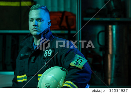 Photo of young fireman looking to camera with helmet in hand near fire truck Photo of young fireman looking to camera with helmet in hand near fire truck 55554927