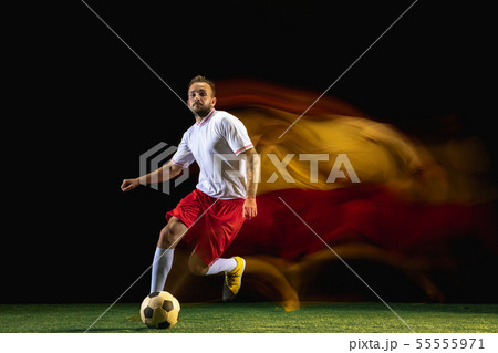 Male soccer player kicking ball on dark background in mixed light 55555971