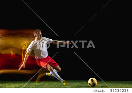 Male soccer player kicking ball on dark background in mixed light Male soccer player kicking ball on dark background in mixed light 55556038