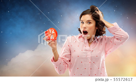 shocked young woman in pajama with alarm clock shocked young woman in pajama with alarm clock 55572617