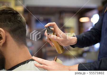 barber applying styling spray to male hair at shop 55573802