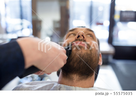 man and barber with trimmer cutting beard at salon man and barber with trimmer cutting beard at salon 55575035