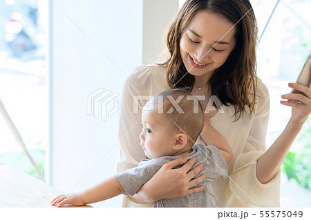 子供を抱きながらスマホを見る女性 55575049