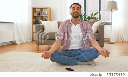 man in headphones meditating in lotus pose at home man in headphones meditating in lotus pose at home 55575439
