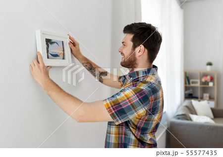 man hanging picture in frame to wall at home 55577435