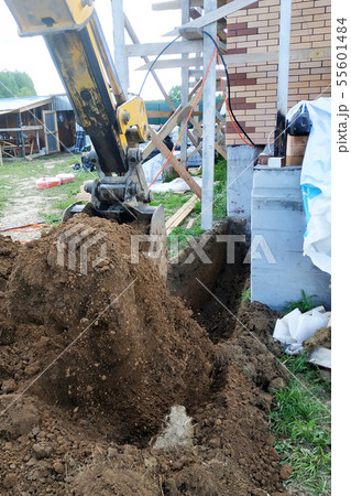 The excavator digs a small trench in the yard. The excavator digs a small trench in the yard. 55601484