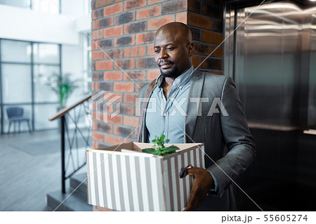 Bearded dark-skinned man leaving office holding box with plant inside Bearded dark-skinned man leaving office holding box with plant inside 55605274