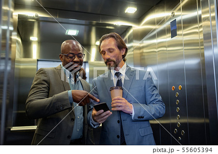 Two businessmen reading info on smartphone while using elevator Two businessmen reading info on smartphone while using elevator 55605394