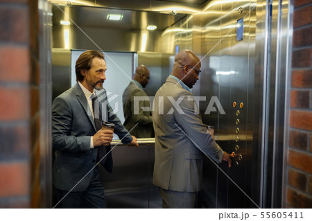 Man pressing button in elevator while standing near colleague Man pressing button in elevator while standing near colleague 55605411