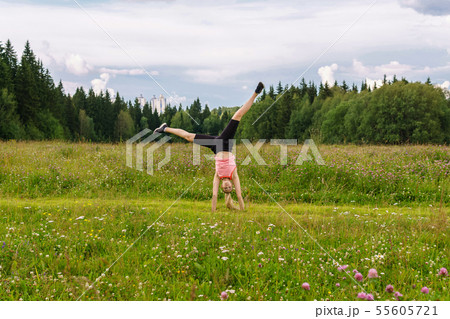 young woman doing exercises cartwheel in a meadow 55605721