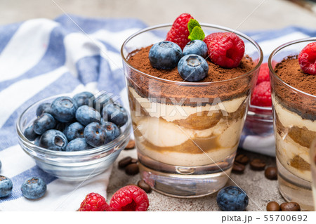 Classic tiramisu dessert with blueberries and raspberries in a glass and napkin on concrete Classic tiramisu dessert with blueberries and raspberries in a glass and napkin on concrete 55700692
