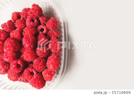 Close-up ripe juicy and delicious raspberry in a plastic transparent dish on a light background Close-up ripe juicy and delicious raspberry in a plastic transparent dish on a light background 55710609