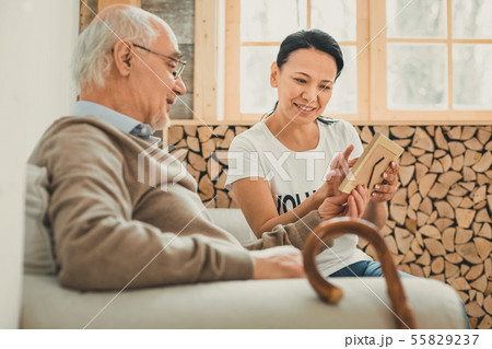 Cheerful dark-haired lady showing photo frame to pensioner 55829237
