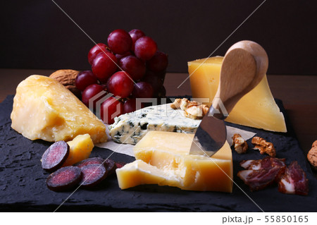 Assorted cheeses, nuts, grapes, fruits, smoked meat and a glass of wine on a serving table. Dark and 55850165