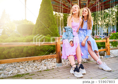 Two girlfriends sit on railing in amusement Park Two girlfriends sit on railing in amusement Park 55907803