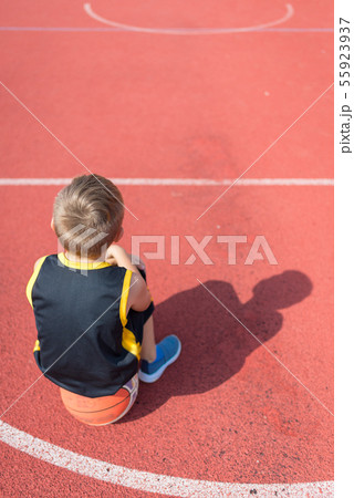 Sad elementary school boy sitting on basketball at 55923937