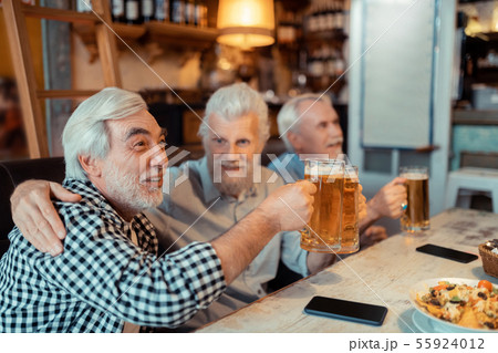 Retired man hugging friend while watching football together Retired man hugging friend while watching football together 55924012