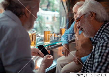 Man showing smartphone while drinking beer with friends Man showing smartphone while drinking beer with friends 55924191