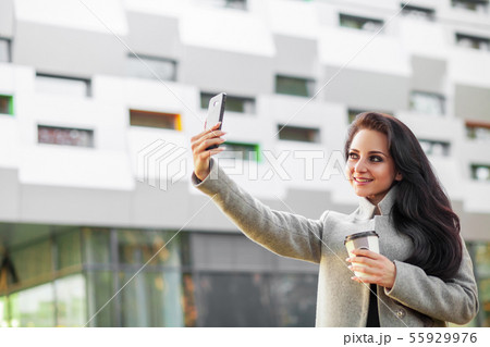 Businesswoman is walking to work in the city. She is holding a coffee cup and is talking on the 55929976