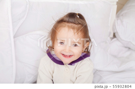 Portrait of baby girl lying in bed under featherbed 55932804