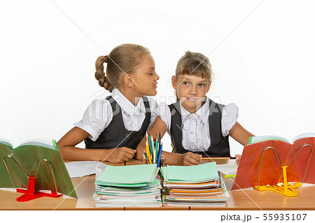 Girls are sitting at a school desk, one whispers 55935107
