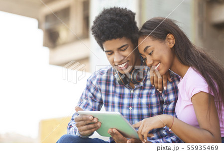 Young couple browsing social media on digital tablet outdoors Young couple browsing social media on digital tablet outdoors 55935469
