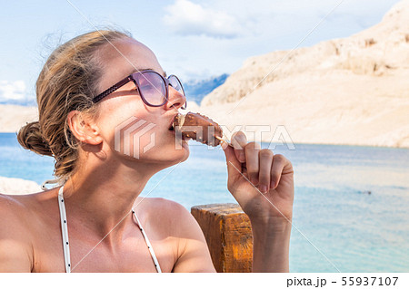 Girl eating icepop in shade on picture perfect beach in summer. Girl eating icepop in shade on picture perfect beach in summer. 55937107