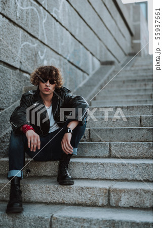 Serious curly rocker sitting on the stone stairs Serious curly rocker sitting on the stone stairs 55937661