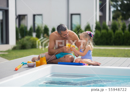 Father and daughter drinking juice while chilling near pool Father and daughter drinking juice while chilling near pool 55948722