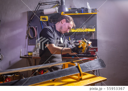 A man in work clothes repairman in the workshop ski service repairing the ski A man in work clothes repairman in the workshop ski service repairing the ski 55953367