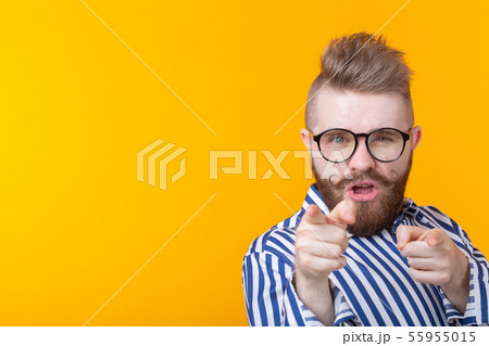 Funny young man with a mustache and a beard and glasses shows on you on a yellow background with Funny young man with a mustache and a beard and glasses shows on you on a yellow background with 55955015