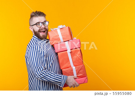 Surprised young hipster guy in glasses holding a large stack of gift boxes on a yellow background Surprised young hipster guy in glasses holding a large stack of gift boxes on a yellow background 55955080