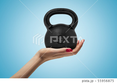 Side closeup of woman's hand facing up and holding big black 32 kg kettlebell on light blue gradient 55956875
