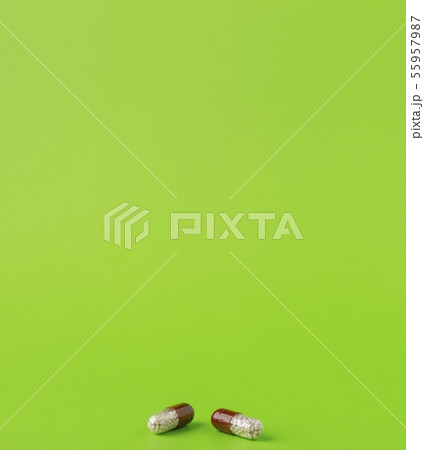 Two brown capsules with medicinal microgranules on a green background. 55957987
