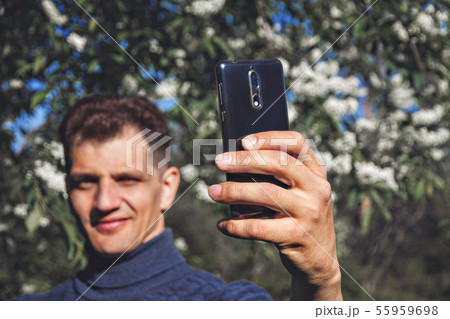 middle-aged man in blue jumper holds holds the phone in front of you, takes selfie in summer park on middle-aged man in blue jumper holds holds the phone in front of you, takes selfie in summer park on 55959698