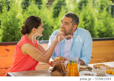 Caring wife smiling while giving some croissant her husband Caring wife smiling while giving some croissant her husband 55981564