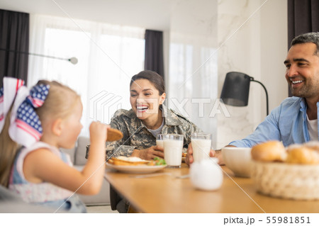 Military woman laughing while looking at her daughter eating cookie Military woman laughing while looking at her daughter eating cookie 55981851