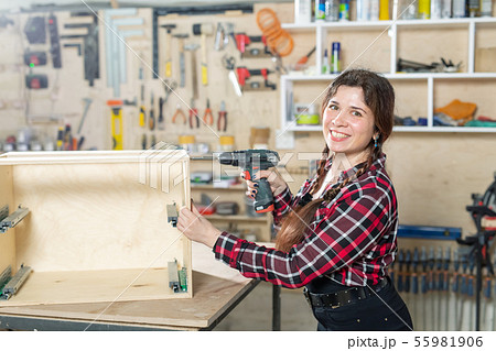 furniture factory, Small-Sized Companies and female worker concept - woman with a drill on the 55981906
